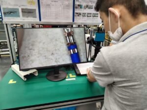 The engineer is inspecting the terminal crimping with a magnifying glass.